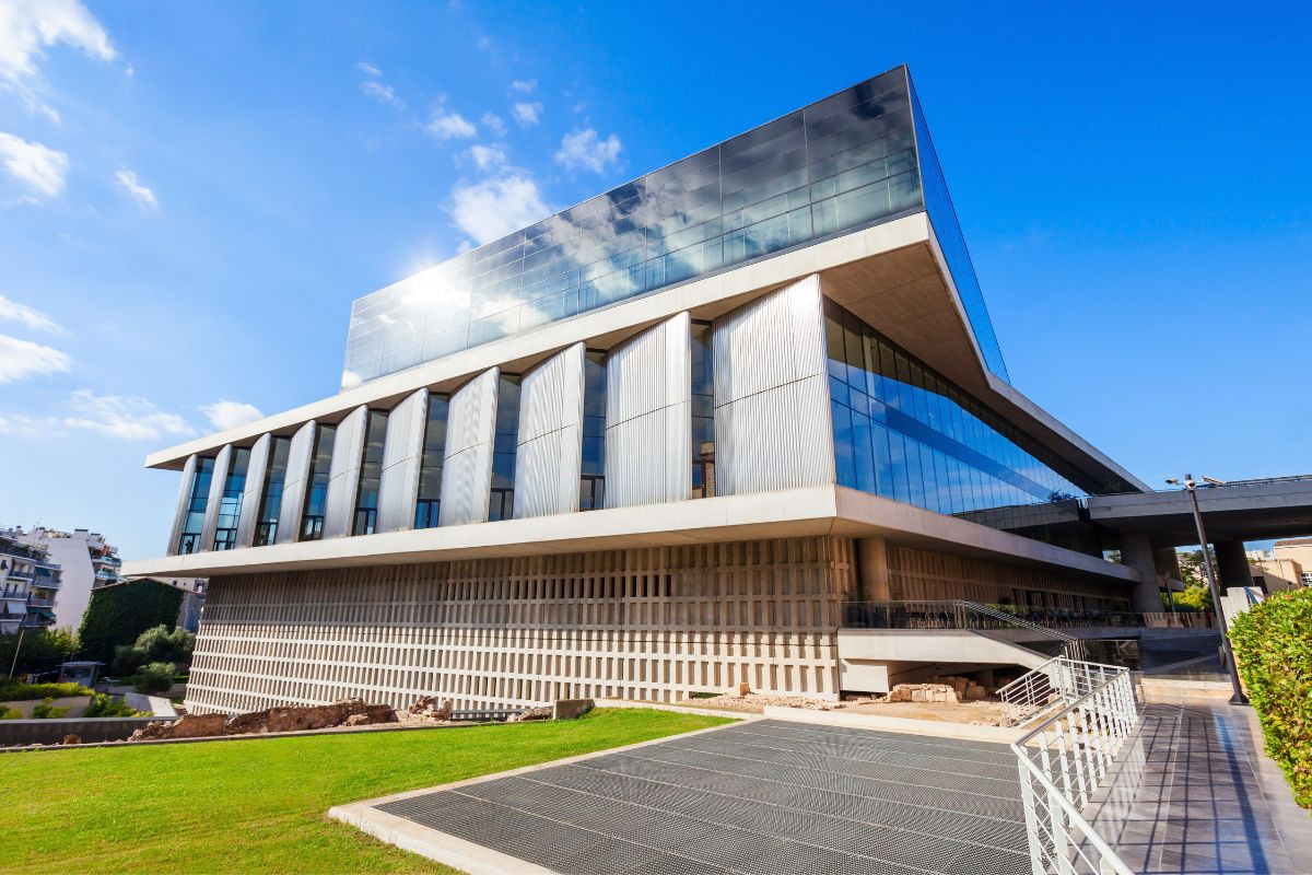 Exterior view of the modern Acropolis Museum with glass walls under a bright sky.